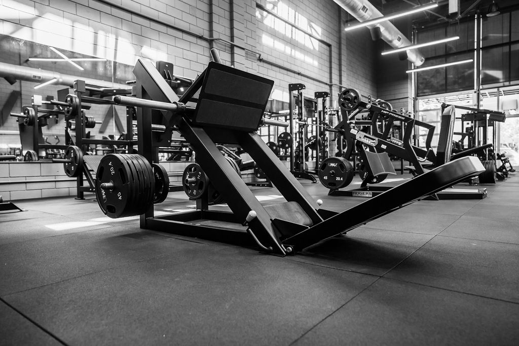 A plate-loaded leg press with benches and racks behind it