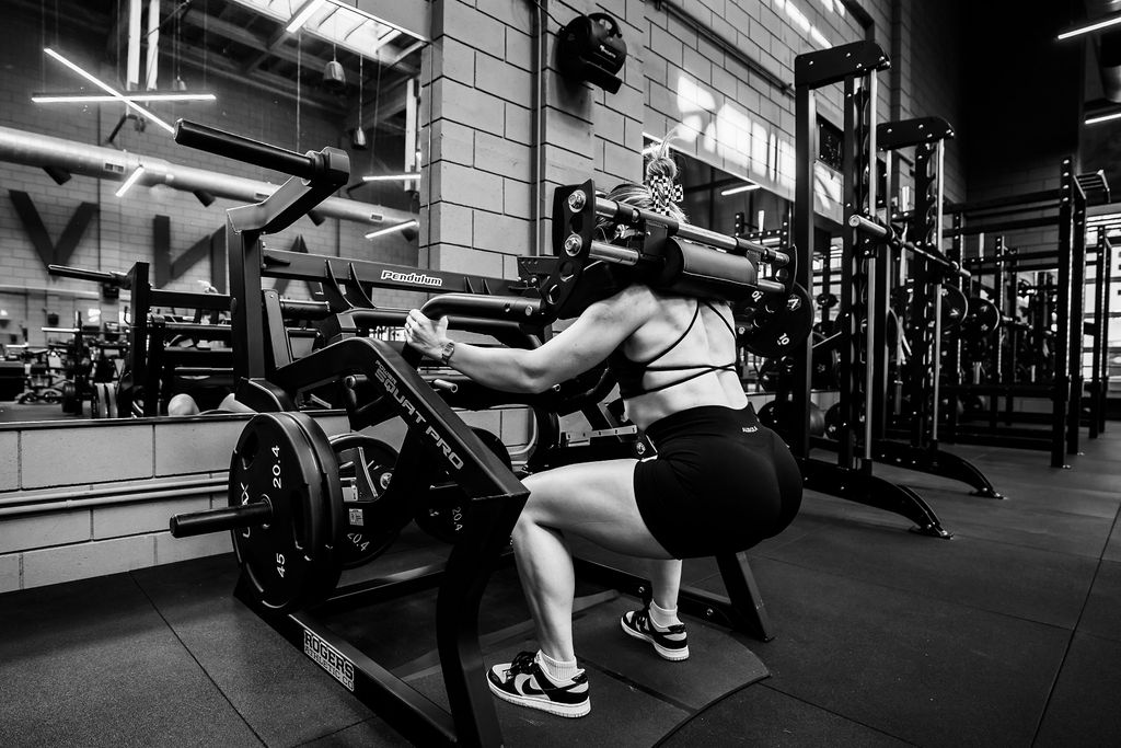 A member training on a plate-loaded squat machine at The Anvil Gym